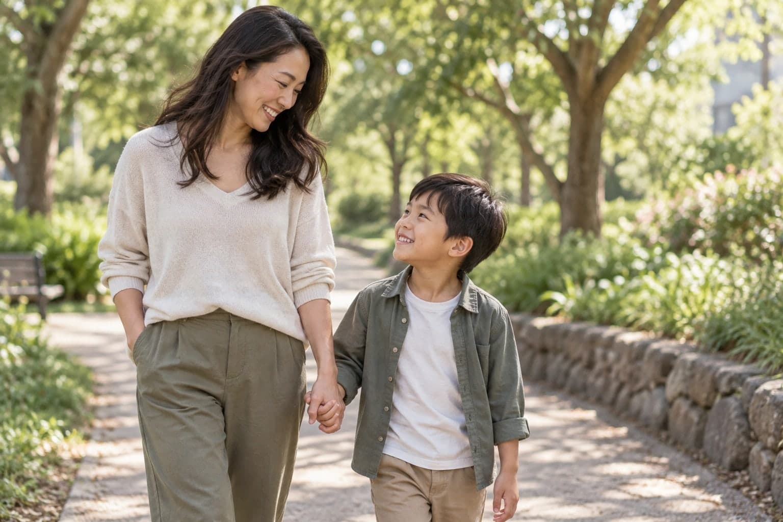 Mãe e filho caminhando de mãos dadas por um parque, sorrindo um para o outro.